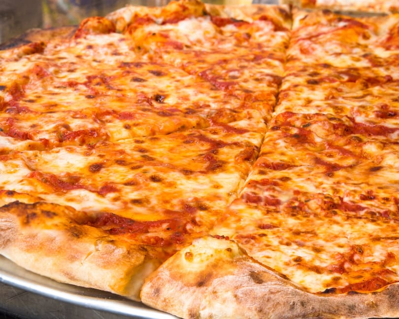 Close-up of a large, freshly baked cheese pizza with a golden crust, sliced and ready to serve.