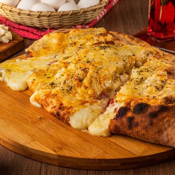Cheesy calzone slices on a wooden board, surrounded by olives, spices, and sauces.