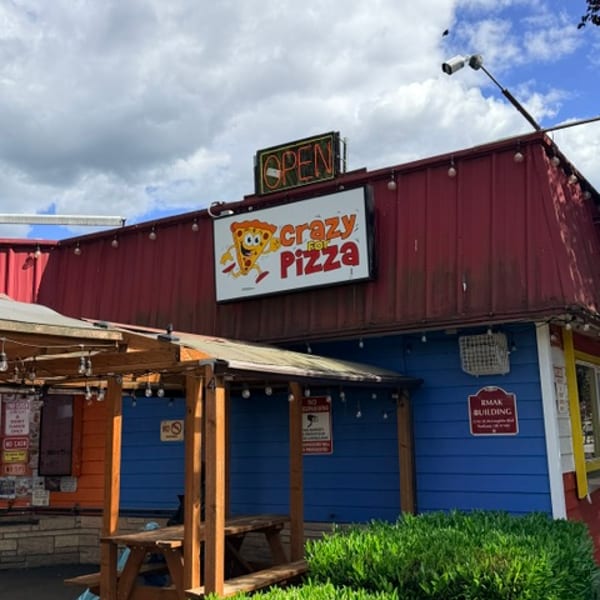 Crazy For Pizza storefront with outdoor seating, signage, and green landscaping.